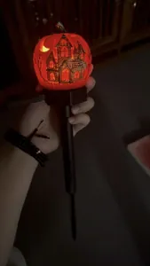 Detailed view of a glowing solar-powered Halloween pumpkin garden stake held by hand