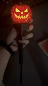 Detailed view of a glowing orange Halloween pumpkin solar stake light held in hand