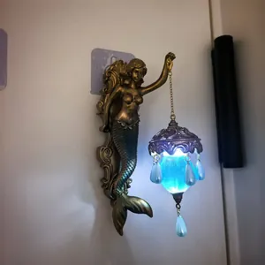 Close-up detail of a vintage bronze mermaid wall lamp featuring a glowing blue hanging lantern