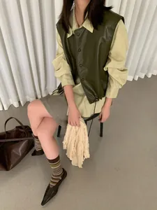 Dettaglio di un gilet in pelle verde oliva vintage abbinato a una sciarpa color crema.
