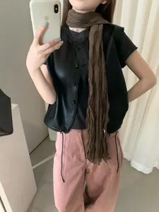 Dettaglio di un gilet in pelle nera vintage con una lunga sciarpa marrone.