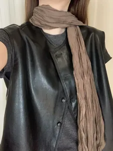 Primo piano di un gilet in pelle nera vintage con una sciarpa marrone coordinata.