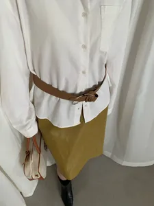 Dettaglio di una camicia in velluto a coste bianca a maniche lunghe con cintura marrone e gonna.