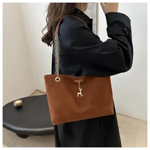 Vista dettagliata della borsa a spalla scamosciata marrone con catena oro e ciondolo.