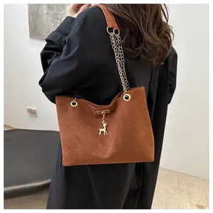 Dettaglio di borsa tote in camoscio marrone con ciondolo a cervo dorato e tracolla.