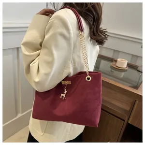 Dettaglio della borsa tote in pelle scamosciata bordeaux con catena dorata e ciondolo cervo