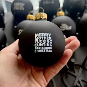 Vue détaillée d'une boule de Noël noire mate amusante tenue à la main avec texte