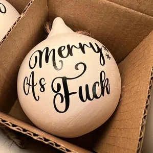 Close-up of a funny white ceramic Christmas bauble with Merry As Fuck text in a box