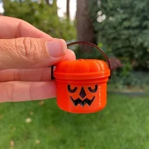 Primo piano di un mini secchiello arancione a forma di zucca di Halloween in mano.