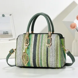 Detalle de bolso tipo almohada tejido a rayas verdes con colgante de hoja y toques dorados
