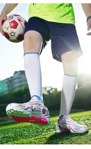 Close-up of youth outdoor turf soccer shoes with pink and black patterns on grass