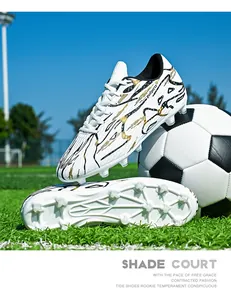 Detailed view of white low-top soccer shoes with black and gold patterns on turf