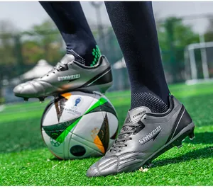 Professional silver soccer cleats with firm ground studs shown on an artificial turf field