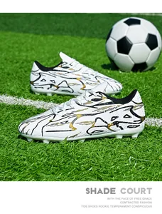 White soccer shoes with black and gold patterns on a green football field