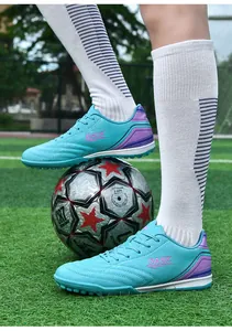 Detail of turquoise turf soccer shoes with cleats on a green field and soccer ball.