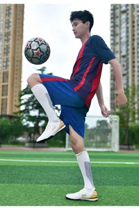 Close-up action shot of white TF turf soccer shoes with gold accents on a green pitch.