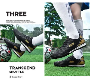 Professional black and gold turf soccer shoes displayed on artificial grass field.