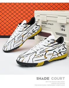Detailed close-up view of white turf soccer shoes with gold and black splash patterns on yellow sole