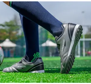 Close-up detail of breathable grey and black turf soccer cleats on a lush green artificial field