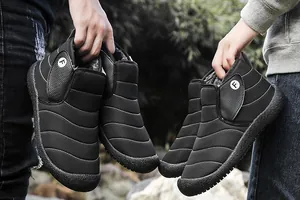 Detail view of two pairs of black quilted snow boots held outdoors by a couple.