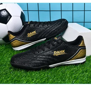 Detailed close-up of black and gold turf soccer shoes presented on artificial grass.