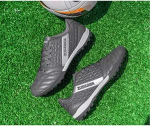 High-quality detail view of grey turf soccer shoes on lush green grass with water droplets