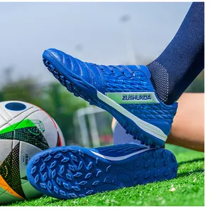 Close-up of blue outdoor turf soccer shoes with ZUSHUNDA logo on artificial grass.