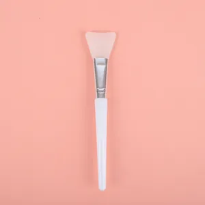 Professional silicone face mask applicator brush with white handle on pink background