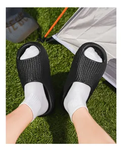 Detail view of black honeycomb textured thick-soled slides worn with white socks on grass