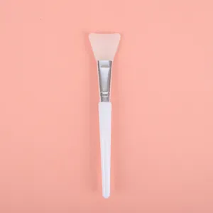Detail view of a soft silicone face mask brush with white handle on pink background