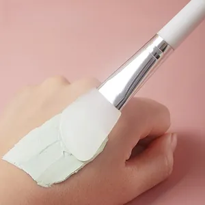 Professional silicone facial mask brush applying green mud mask on hand for skincare routine