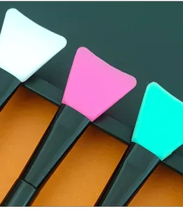 Close-up detail of colorful silicone facial mask brushes featuring sleek black handles.