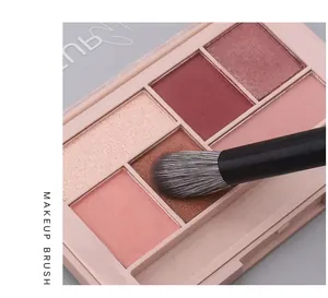 Primer plano de un pincel de maquillaje profesional en una paleta de sombras rosa suave