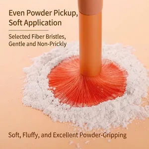 Macro shot of a soft fiber makeup brush picking up loose powder on a warm peach background