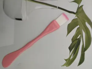 Close-up of pink dual-use facial mask brush and spatula with soft white fiber bristles