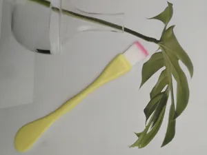 Close-up of yellow dual-use facial mask brush with pink tipped bristles