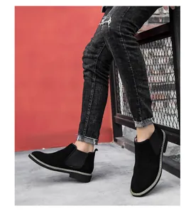 Detail view of men's black suede Chelsea boots worn with distressed black denim jeans.