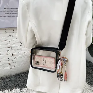 Dettaglio di una borsa a tracolla in PVC trasparente con tracolla larga e sciarpa decorativa.