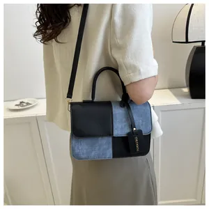 Sac à main élégant en denim et cuir noir effet patchwork porté à l'épaule par une femme