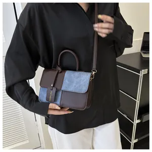Détail d'un sac à main élégant en cuir marron et panneaux en denim bleu texturé contrasté.
