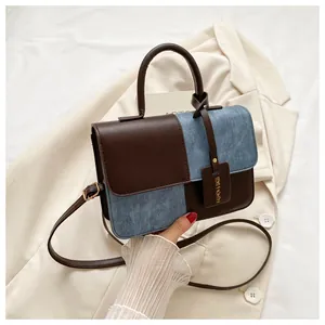 Détail d'un sac à main patchwork élégant en cuir marron et denim bleu sur un blazer blanc.