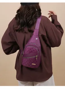Detail view of a purple quilted sling bag worn by a model on a beige background.