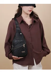 Detail view of a stylish black quilted sling bag worn by a female model in brown shirt.