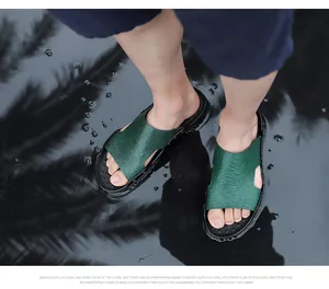 Detail of men's green crocodile-patterned slippers worn on wet ground with palm tree reflections