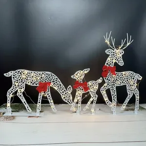 Close-up of three white iron Christmas reindeer with red bows and warm LED lights.