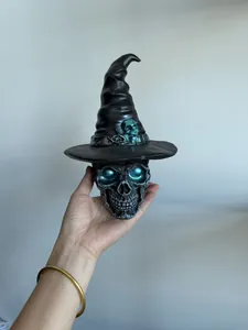 Detailed view of gothic skull figurine with witch hat and glowing teal eyes held in hand