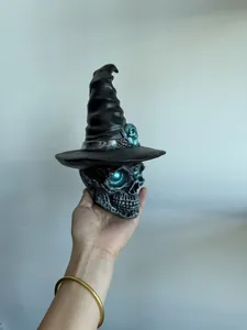 Handheld view of a gothic resin skull wearing a black witch hat with blue glowing eyes