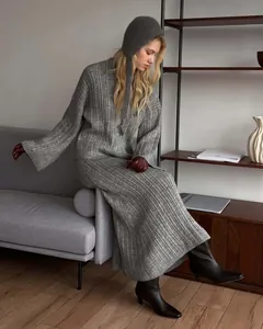 Model wearing a grey ribbed knit sweater and long skirt set in a modern home interior.