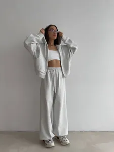 Model draagt een grijze oversized hoodie met rits en bijpassende wijde joggingbroek