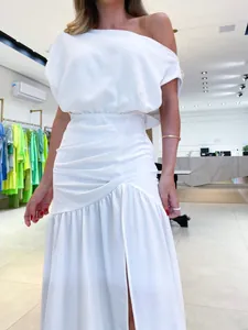 Detail of elegant white one-shoulder maxi dress with pleated waist and high side slit